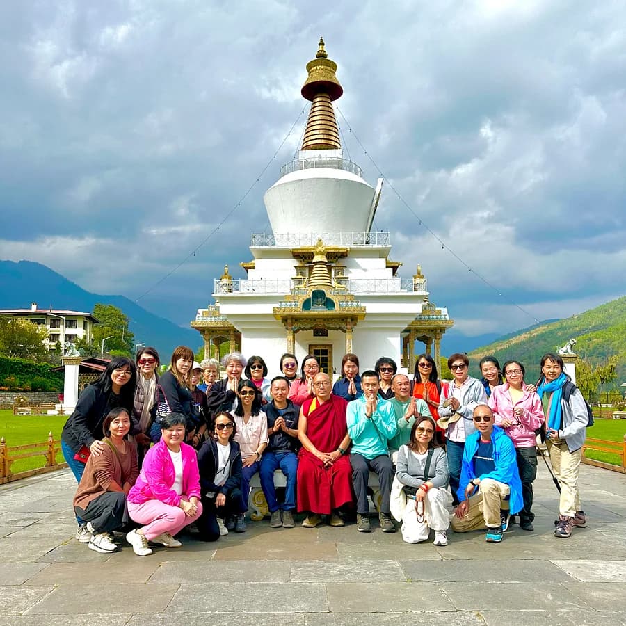 A large group photo at the National Memorial Chorten in Thimphu, with a monk seated among the travelers